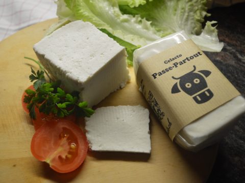 Passe-Partout, eine Art Käse aus Molke, aufgeschnitten links, rechts verpackt, dahinter Salat, vorne links eine aufgeschnittene Tomate und Petersilie