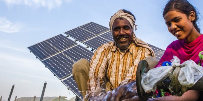 Ein Mann und eine Frau in Südasien vor einem Solarpanel, das eine Wasserpumpe betreibt